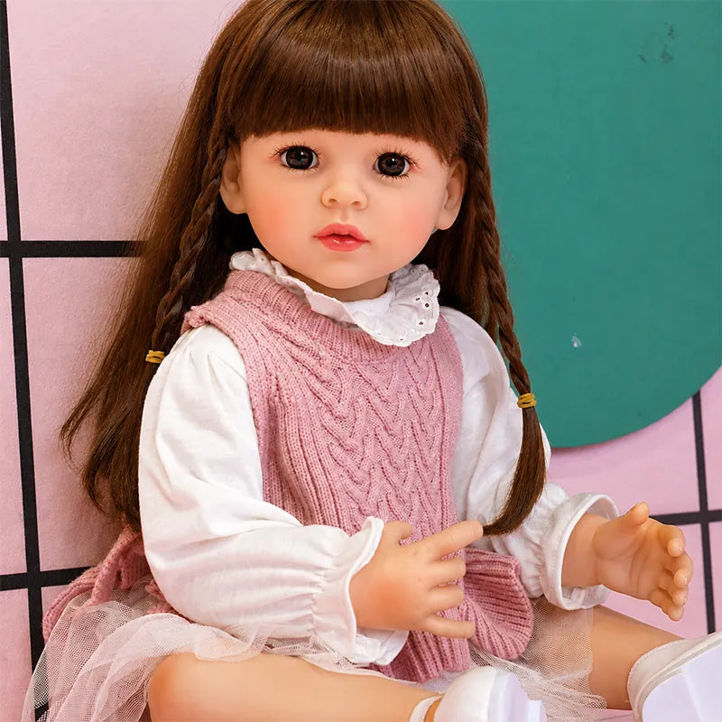 Realistic reborn girl doll with lifelike brown eyes, long brunette hair, and a sweet pink knitted outfit.