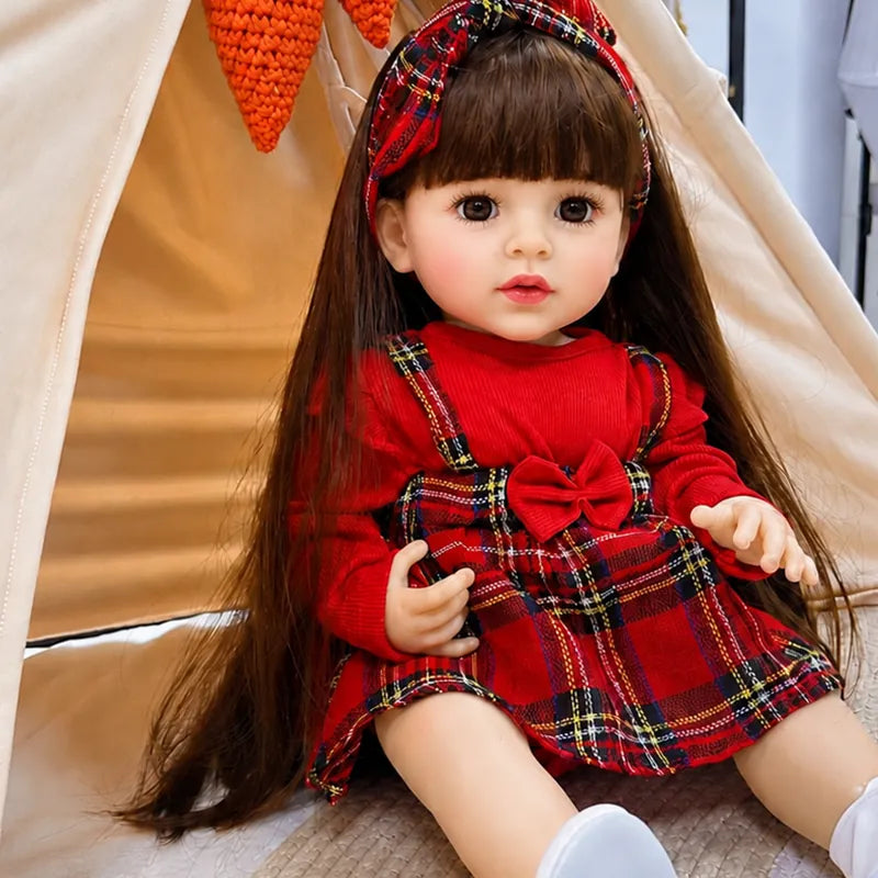 Lifelike reborn baby doll with long brown hair, realistic facial details, expressive brown eyes, and a charming red plaid outfit.