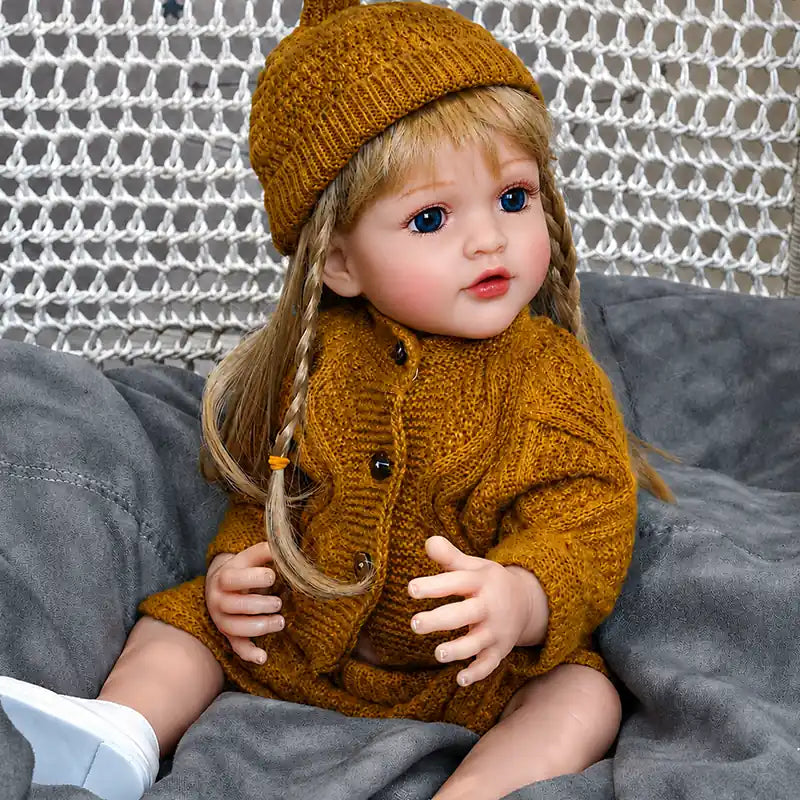 Lifelike reborn baby doll with blue eyes, realistic facial details, long hair, rosy cheeks, and a cozy knitted outfit for play or collecting.