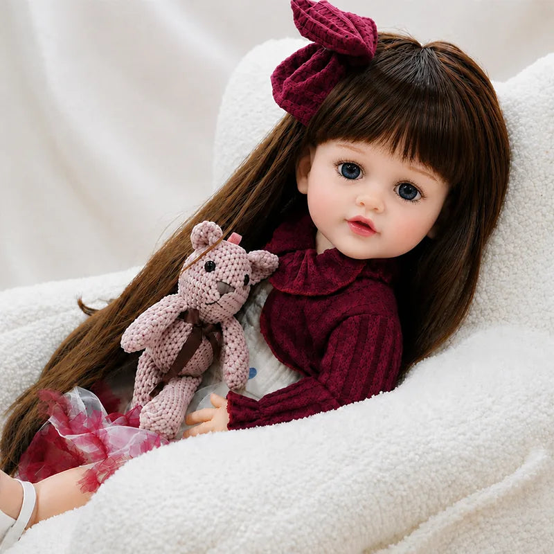 Realistic reborn baby girl doll with long brown hair, expressive eyes, burgundy dress and lifelike facial details for imaginative play and collecting.
