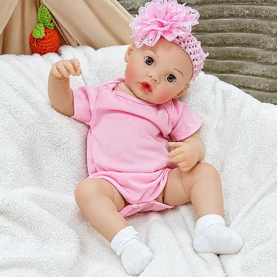 Sweet reborn baby doll with a playful pink outfit, floral headpiece, rosy cheeks, bright eyes, and feeding functionality, ideal for collectors and gift giving.