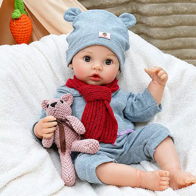 Clara wears a blue bear-ear hat, matching romper, and red knitted scarf, with rosy cheeks, bright brown eyes, tiny toes, and a cuddly teddy bear.