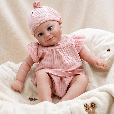 Eliza realistic reborn baby doll in a pink ruffled outfit and matching knotted hat, seated on a cream blanket.