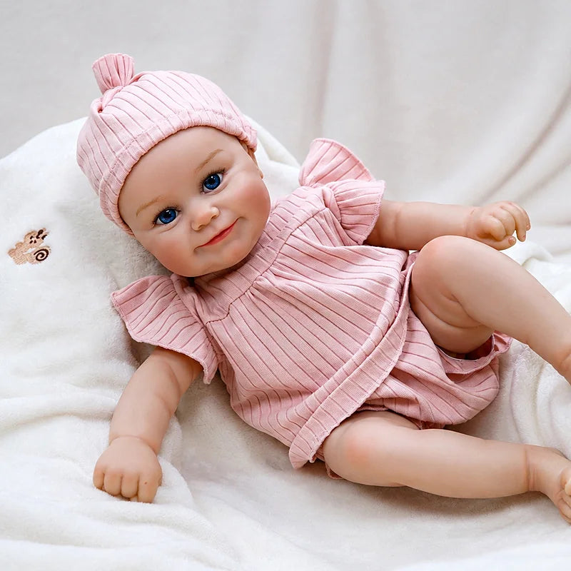 Eliza reborn baby doll in a matching pink outfit and hat, resting against soft cream bedding with animal motifs.