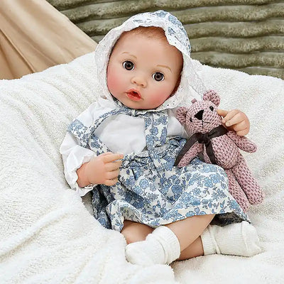 Ellis relaxes on a soft blanket with a teddy bear, ready for bottle time, bedtime stories, pretend parenting, and warm family moments.