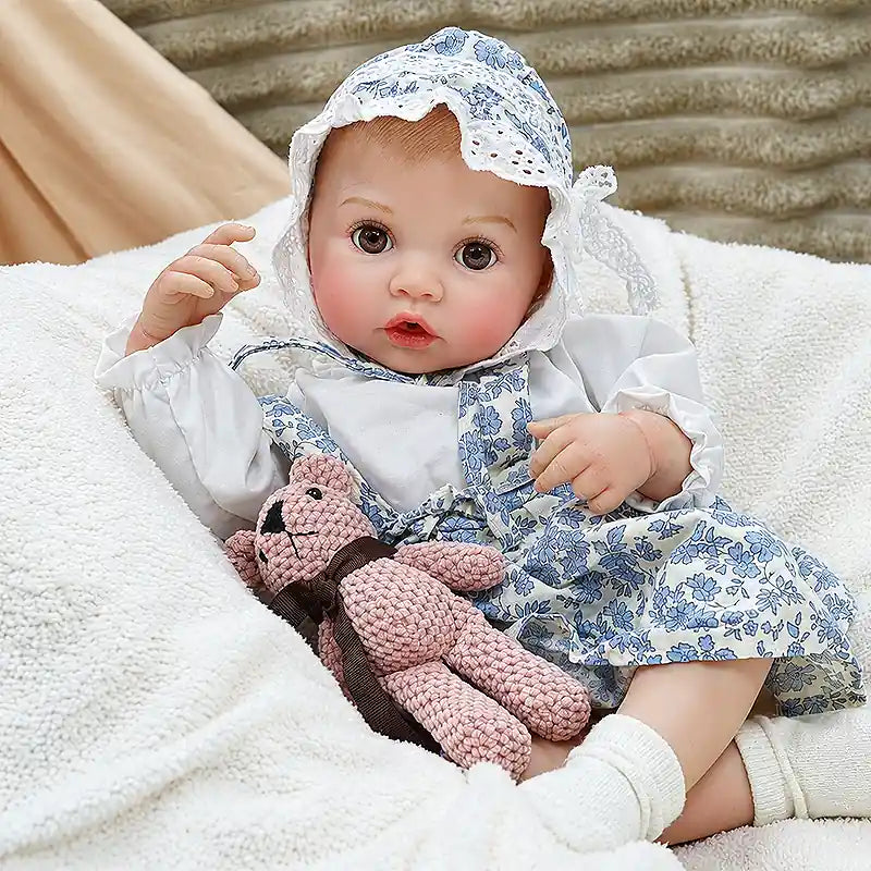 Ellis wears a blue floral romper, matching bonnet, and white socks, featuring bright eyes, rosy cheeks, tiny fingers, and lifelike baby details.