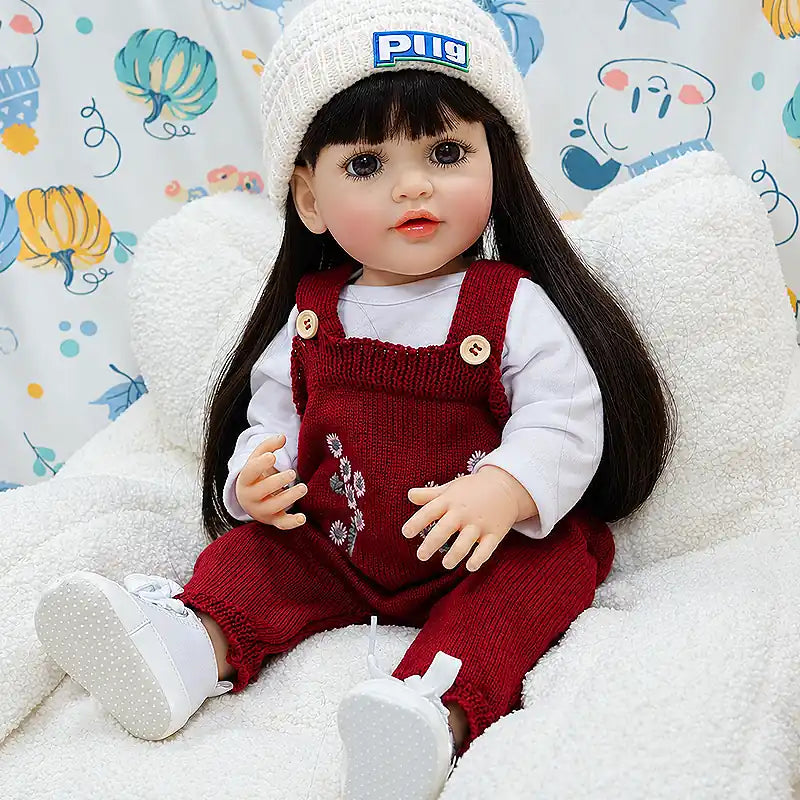 Lifelike reborn girl doll Charlotte with long dark hair, bright brown eyes, rosy cheeks, soft lips, and carefully detailed hands, seated on a fluffy blanket ready for storytime.