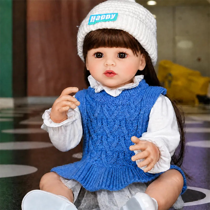 Fashionable reborn baby girl doll wearing a blue cable-knit dress, white ruffled blouse, knit beanie, and matching shoes.