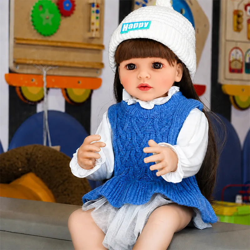 Realistic reborn baby girl doll with long brown hair, expressive brown eyes, and a stylish blue knitted outfit.