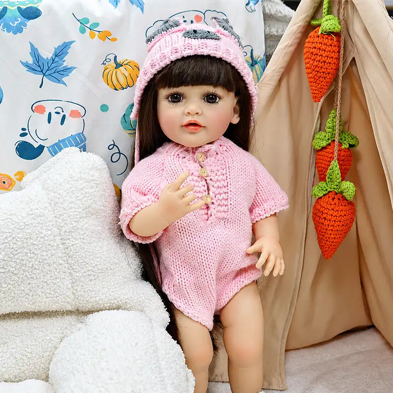 Collectible reborn doll featuring finely painted facial details, glossy lips, realistic eyelashes, long rooted brown hair, and a textured pink handmade knit set.