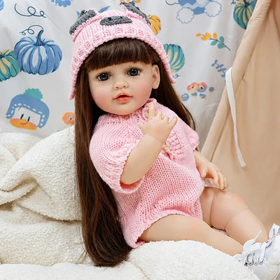 Adorable reborn girl doll sitting comfortably on a fluffy blanket, dressed in a pink romper and animal-themed knit hat, perfect for pretend play, collecting, and nursery display.