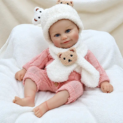 Soft vinyl reborn baby doll in a pink knit outfit and fluffy white bear hat.