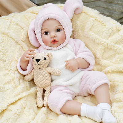 Realistic reborn baby Ella in a soft pink bunny outfit, designed for bottle-feeding play with expressive eyes, delicate hands, rosy cheeks, and a cuddly teddy bear.