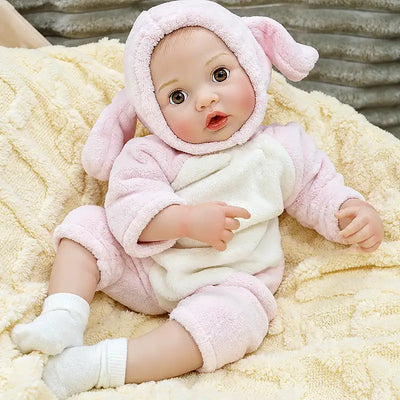 Lifelike baby doll Ella with a bottle-feeding feature, adorable bunny hood, gentle facial details, tiny fingers, and a cozy pose on a soft blanket.