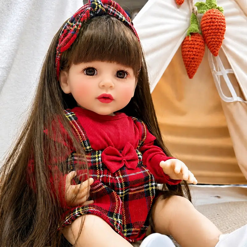 Cute reborn girl doll with extra-long brown hair, plaid bow headband, red tartan dress, bright eyes, and a sweet lifelike expression.