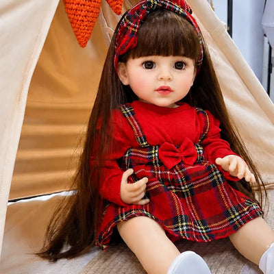 Lifelike reborn baby doll with long brown hair, realistic facial details, expressive brown eyes, and a charming red plaid outfit.