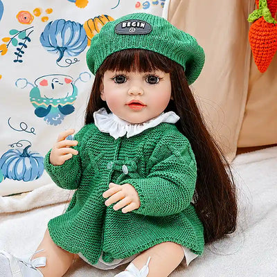 A sweet reborn girl doll Amelia sitting on a soft blanket in a cozy play tent, dressed in textured green knitwear with tiny white shoes, ready for storytime adventures.