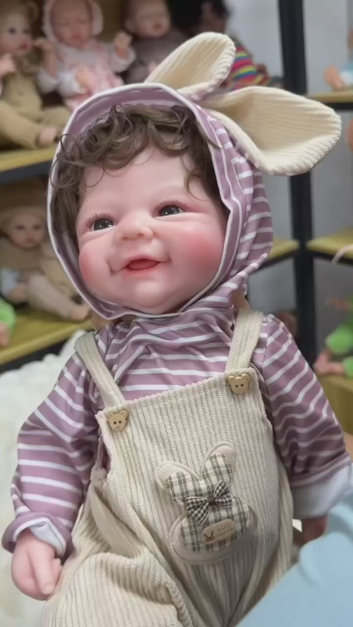 Load video: Full Silicone Reborn Baby Doll Wearing a Striped Hooded Outfit and Cream Knitted Overalls with a Sweet Happy Smile