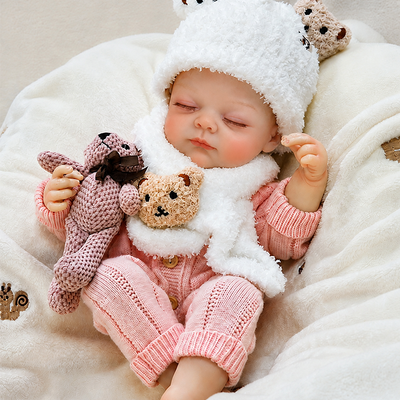 Sleeping reborn baby doll dressed in a pink knit outfit, fluffy white hat and scarf, creating a warm and charming winter nursery look.