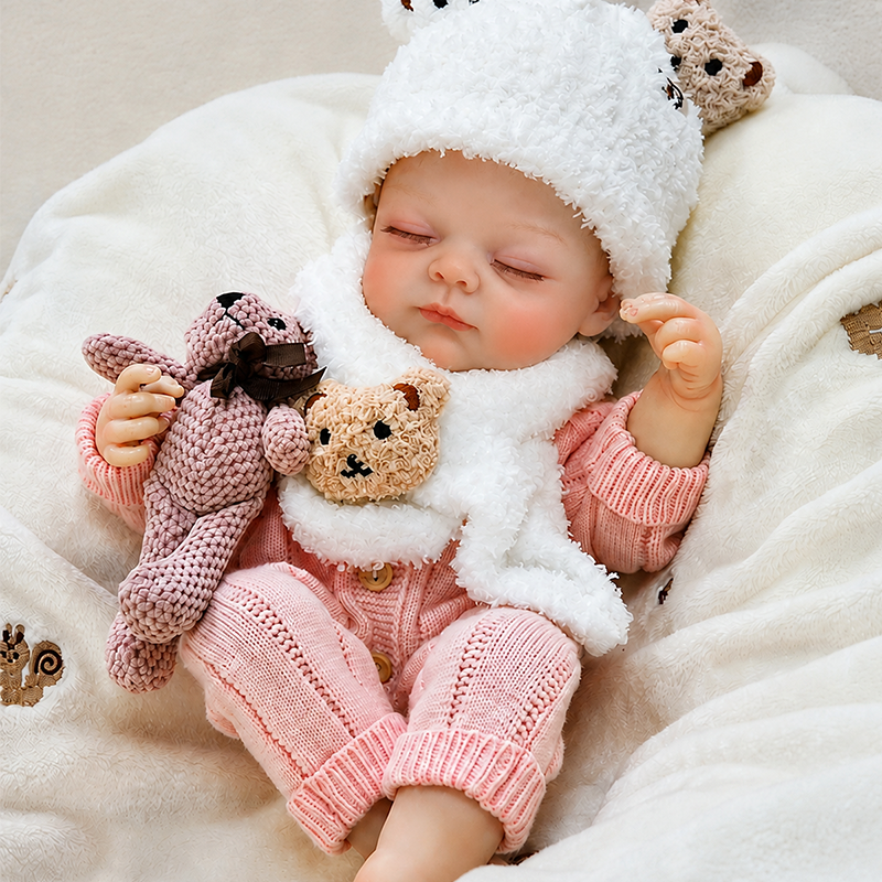 Sleeping reborn baby doll dressed in a pink knit outfit, fluffy white hat and scarf, creating a warm and charming winter nursery look.