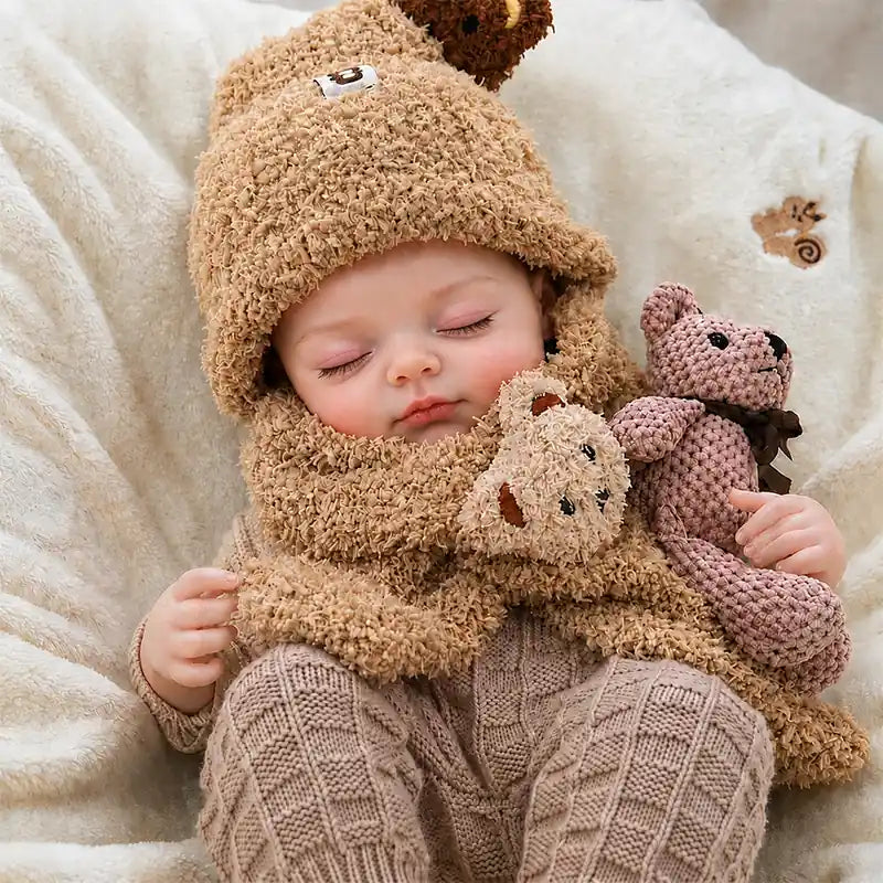 Sweet reborn baby doll curled up under a soft blanket in warm neutral knitwear, creating a peaceful bedtime-inspired nursery scene.