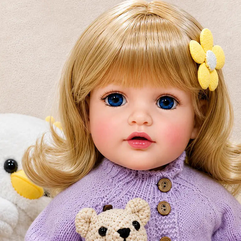 Close-up style reborn doll with vivid blue eyes, glossy pink lips, soft blush, detailed eyelashes, and neatly styled blonde bangs.
