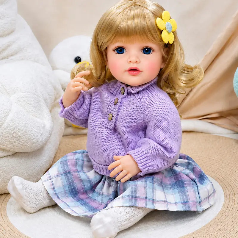 Cute reborn girl doll wearing a lavender knitted sweater, purple plaid skirt, white socks, and yellow flower hair clip.