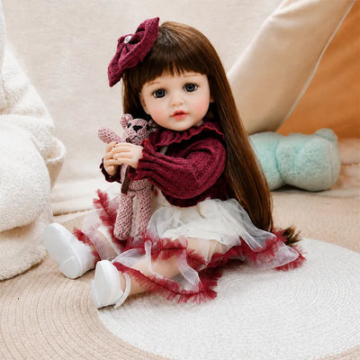 Reborn girl doll wearing an elegant burgundy lace top and layered tulle skirt while holding a cute knitted animal toy for charming pretend play.