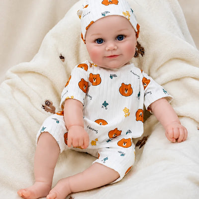 Smiling reborn baby doll in a cute bear-print romper and matching cap, ideal for birthdays, Christmas gifts, nursery displays, and pretend play.