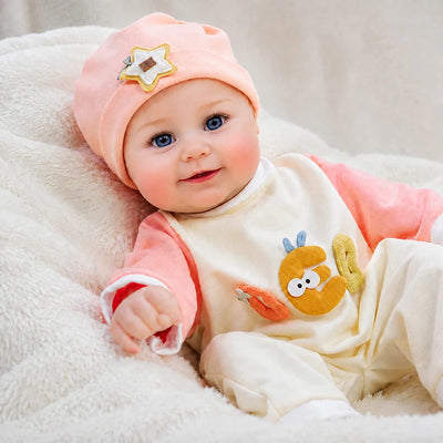 Close-up style view of a reborn doll with sparkling blue eyes, softly painted eyebrows, rosy cheeks, natural pink lips, and a cheerful baby expression.