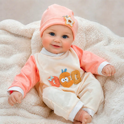 Realistic reborn baby doll with bright blue eyes, rosy cheeks, a sweet smile, and a soft peach outfit with matching baby hat.